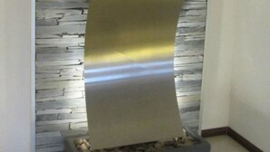 Una pared moderna con un estampado de piedra texturizada y una gran escultura curva de metal.