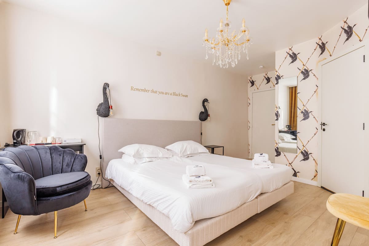A bedroom with a large bed, a chair, a chandelier, and a wall with a bird pattern.