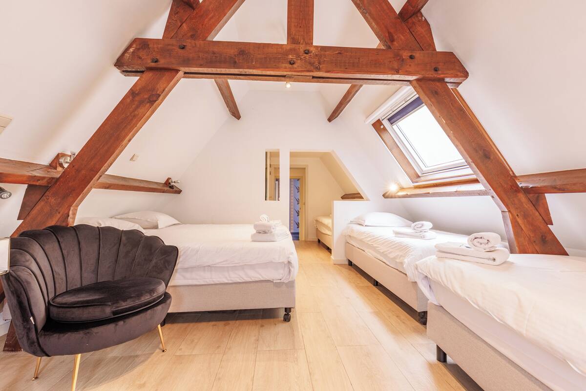 A room with two beds, a black chair, wooden beams, and a skylight.