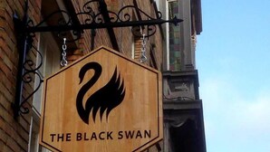 Un letrero hexagonal con el logotipo de un cisne negro y el texto "THE BLACK SWAN" colgado de un edificio.