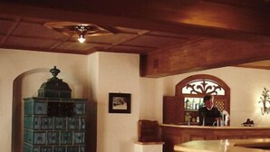 A cozy room with a wooden ceiling, a bookshelf, a small table, and a decorative mirror. - Hotel Gasthof Moosleitner (Freilassing)