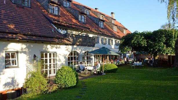 A traditional European-style building with a courtyard. There are outdoor seating areas with umbrellas, and people are dining and socializing. - Hotel Gasthof Moosleitner (Freilassing)