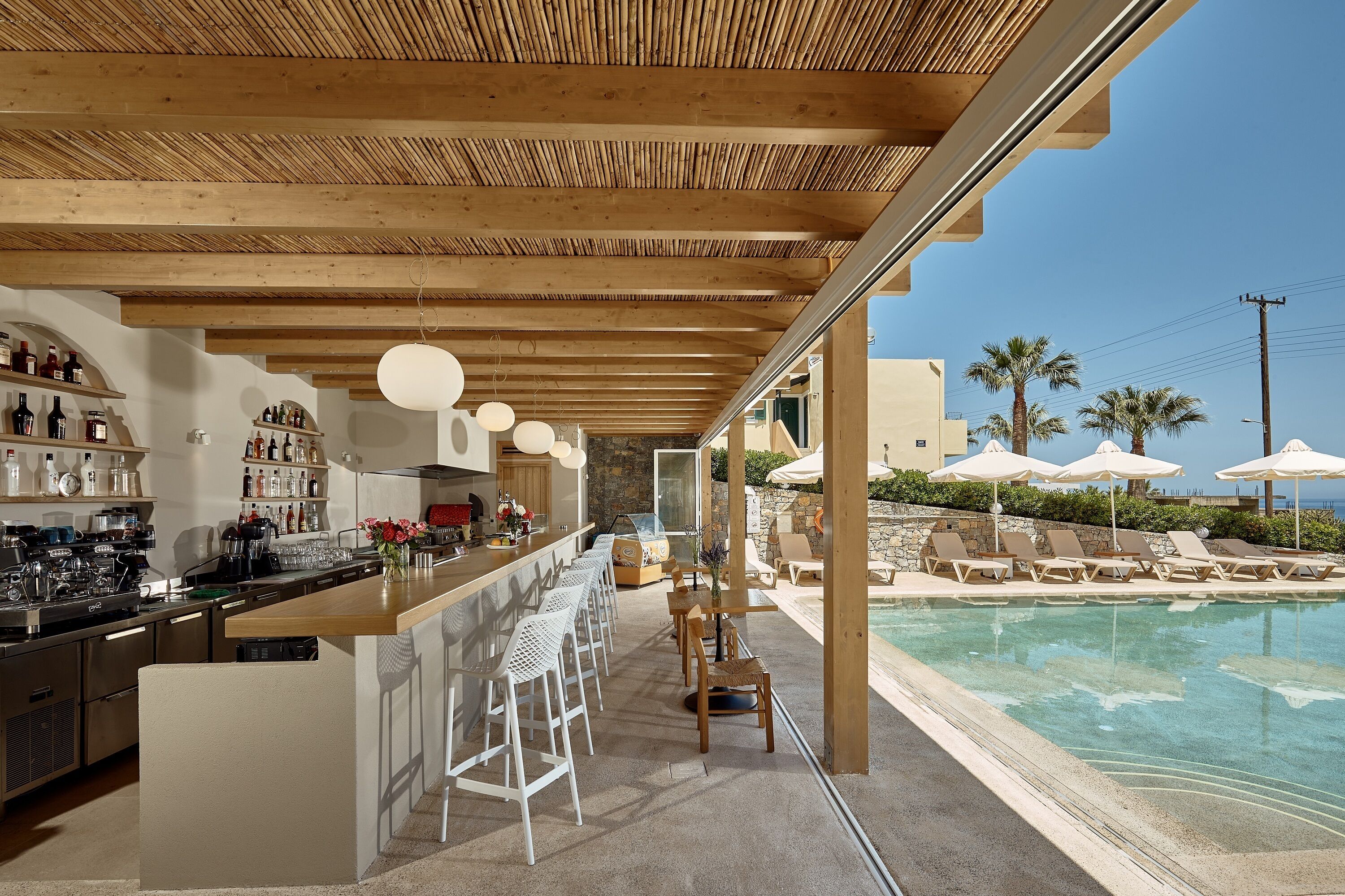 A modern kitchen with bar stools and a poolside area with lounge chairs and umbrellas.