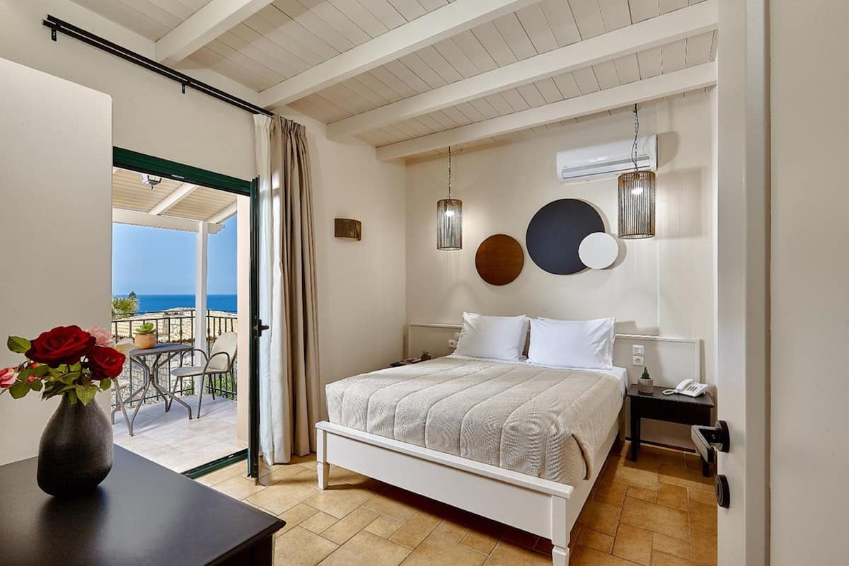 A bedroom with a bed, bedside table, and a view of the sea through an open door.
