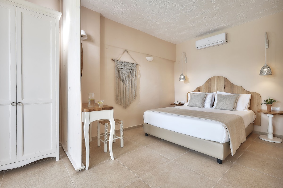 A bedroom with a bed, bedside table, chair, wardrobe, and a wall-mounted air conditioner.
