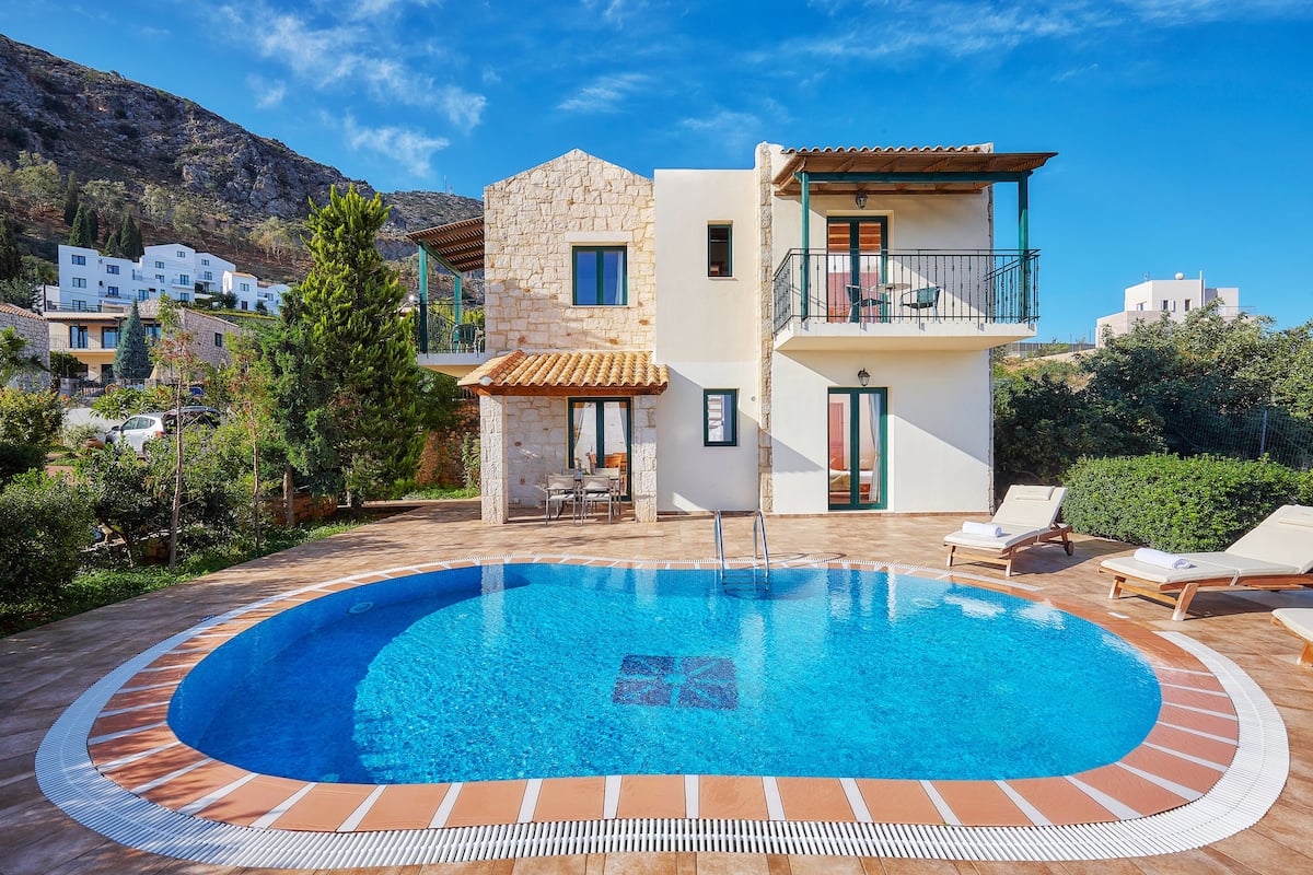 A modern two-story building with a swimming pool, outdoor seating, and a view of the surrounding landscape.