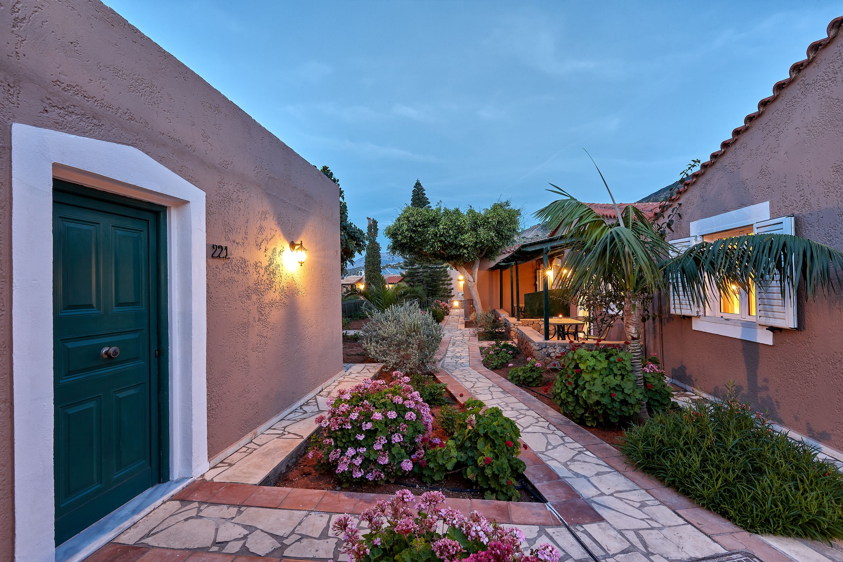 A courtyard with a green door, numbered 221, surrounded by well-maintained gardens and a stone pathway.