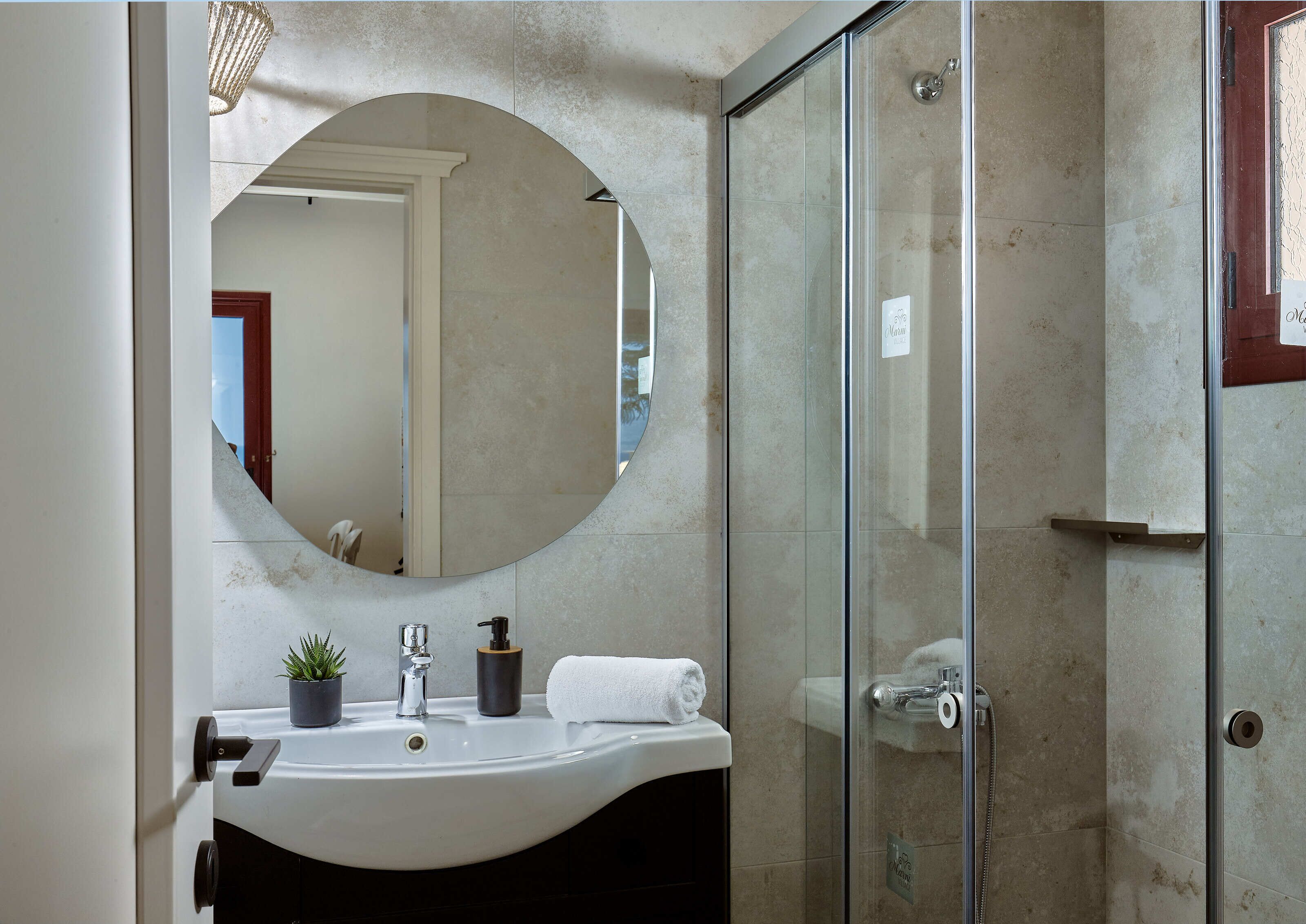 A bathroom with a large mirror, a sink, a shower, and a potted plant.