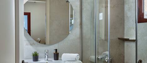 A bathroom with a large mirror, a sink, a shower, and a potted plant.