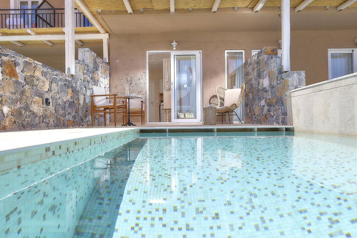 A swimming pool with mosaic tiles, stone walls, and a wooden deck with chairs.