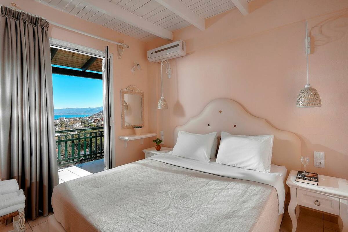 A bedroom with a large bed, a nightstand, a bedside table, a mirror, and a view of the city through a balcony.