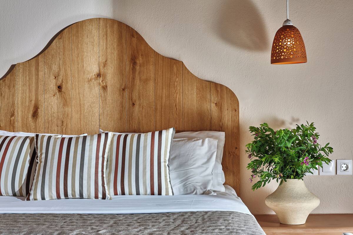 A bed with striped pillows, a wooden headboard, a hanging light fixture, and a potted plant.
