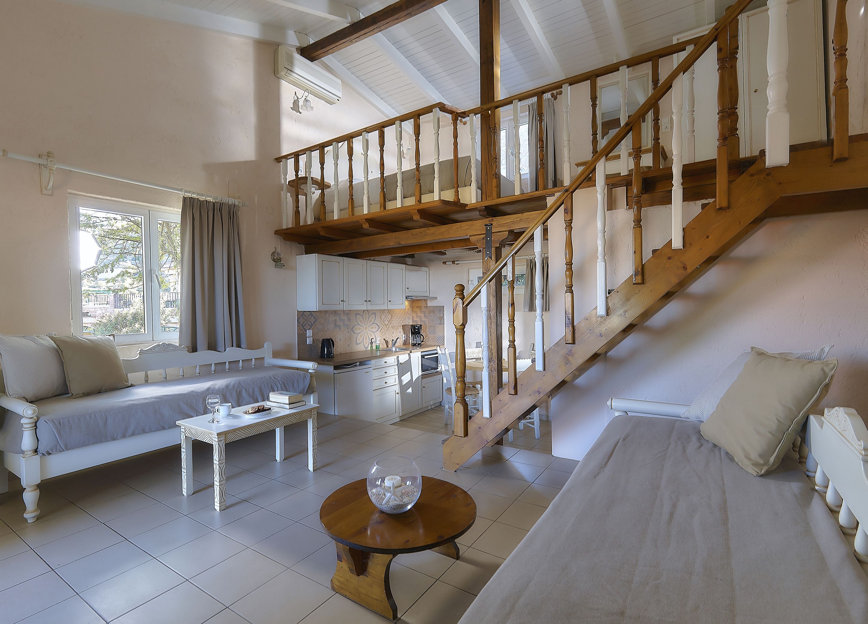 A spacious living area with a wooden staircase, a sofa, a dining table, and a kitchen in the background.