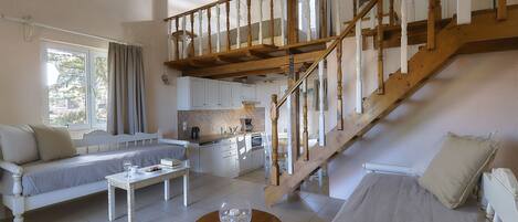 A spacious living area with a wooden staircase, a sofa, a dining table, and a kitchen in the background.