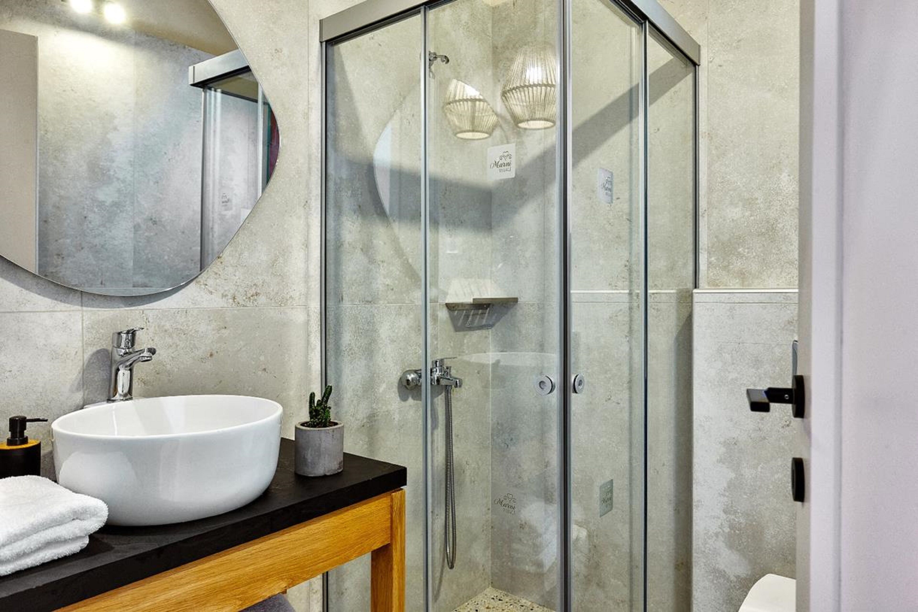 Un bagno moderno con un ampio lavandino bianco, un mobile contenitore in legno, una cabina doccia in vetro e un grande specchio.