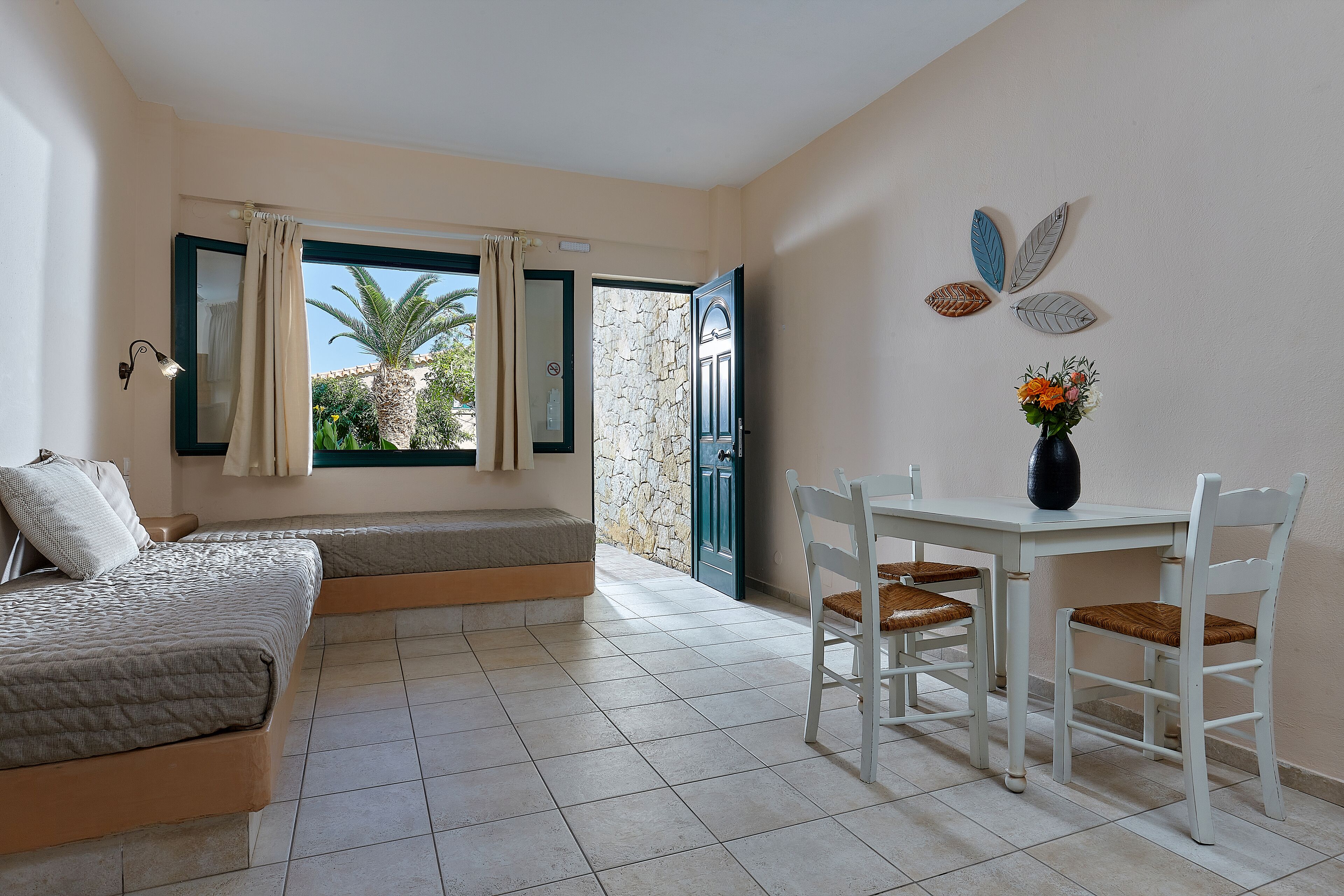 A bedroom with a bed, a small table with chairs, a window with curtains, and a view of the outside.