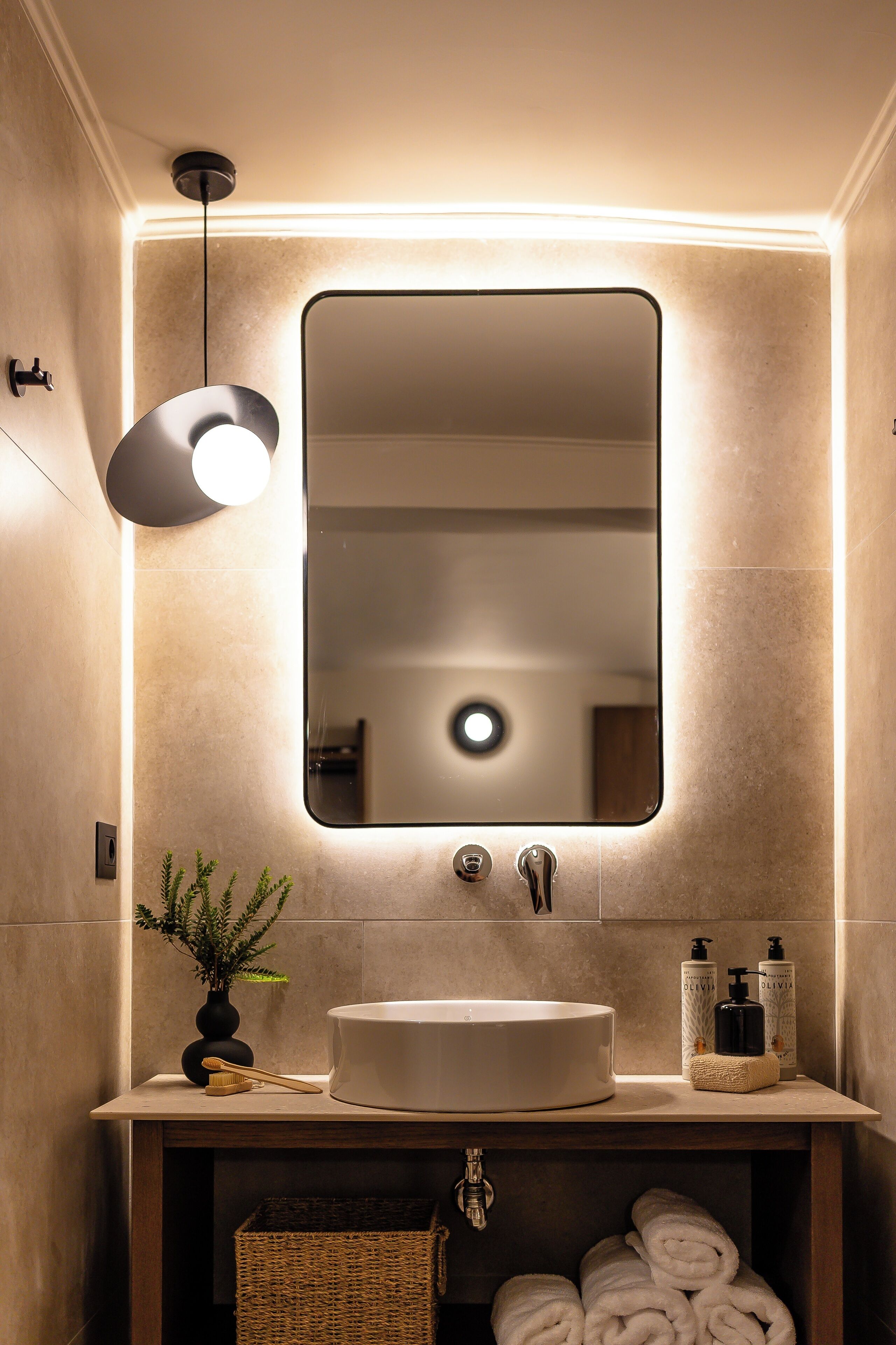 A modern bathroom with a large mirror, a round sink, and a hanging light fixture.