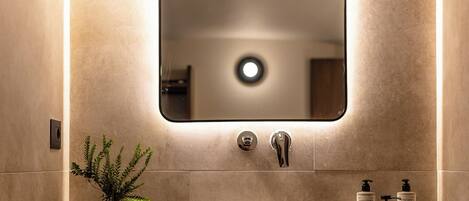 A modern bathroom with a large mirror, a round sink, and a hanging light fixture.