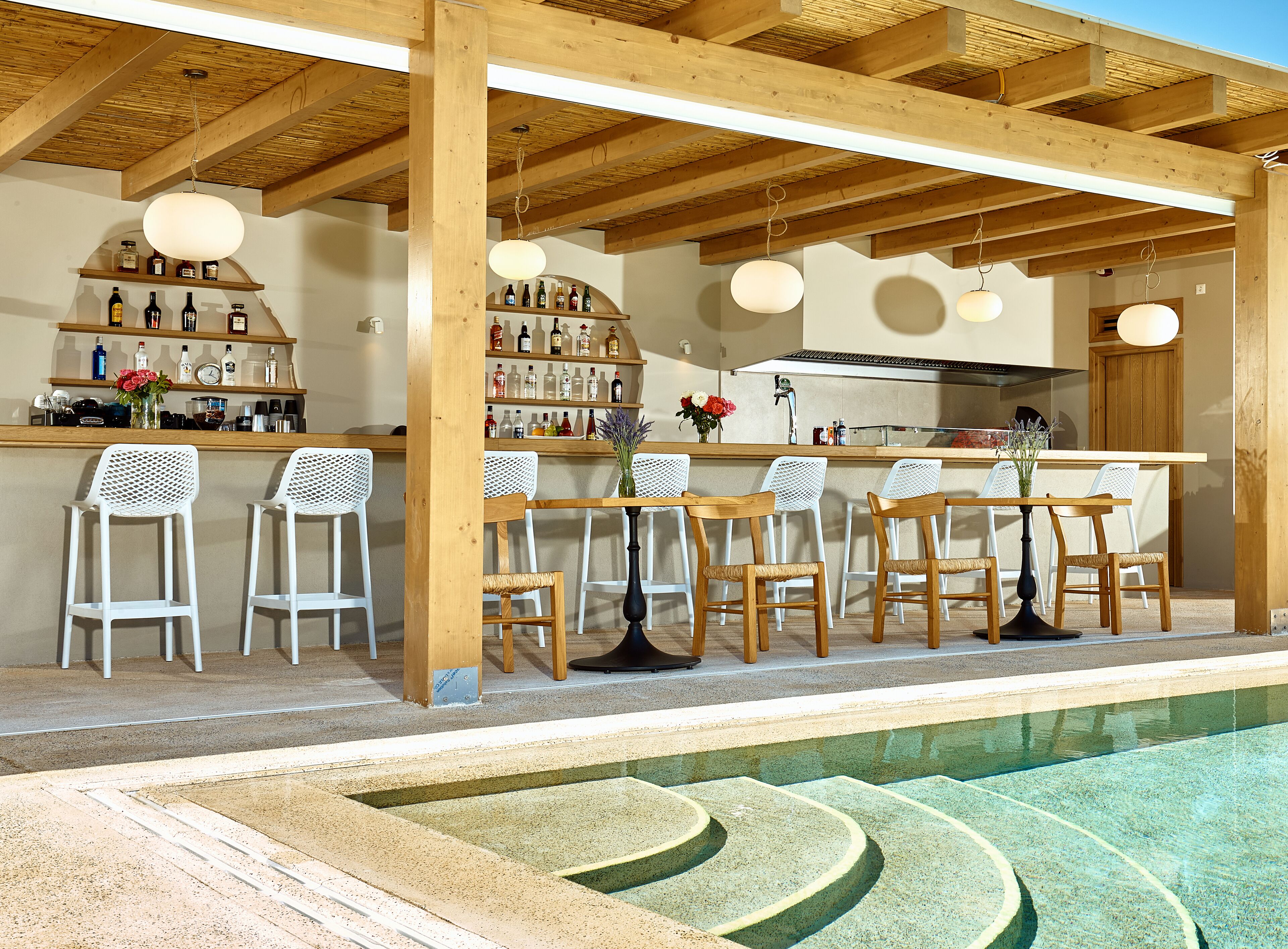 Eine Bar mit Holzbalken, weißen Barhocker und einem Pool mit geometrischem Muster.