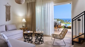 A modern living room with a sofa, two side tables, a lamp, and a wicker chair. A staircase leads to an outdoor area with a pool and a view of the ocean. - Marni Village (Hersonissos)