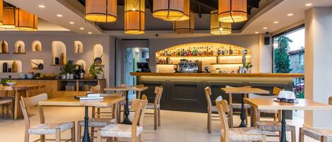 A modern restaurant with wooden tables and chairs, a bar area with a variety of bottles, and pendant lighting.