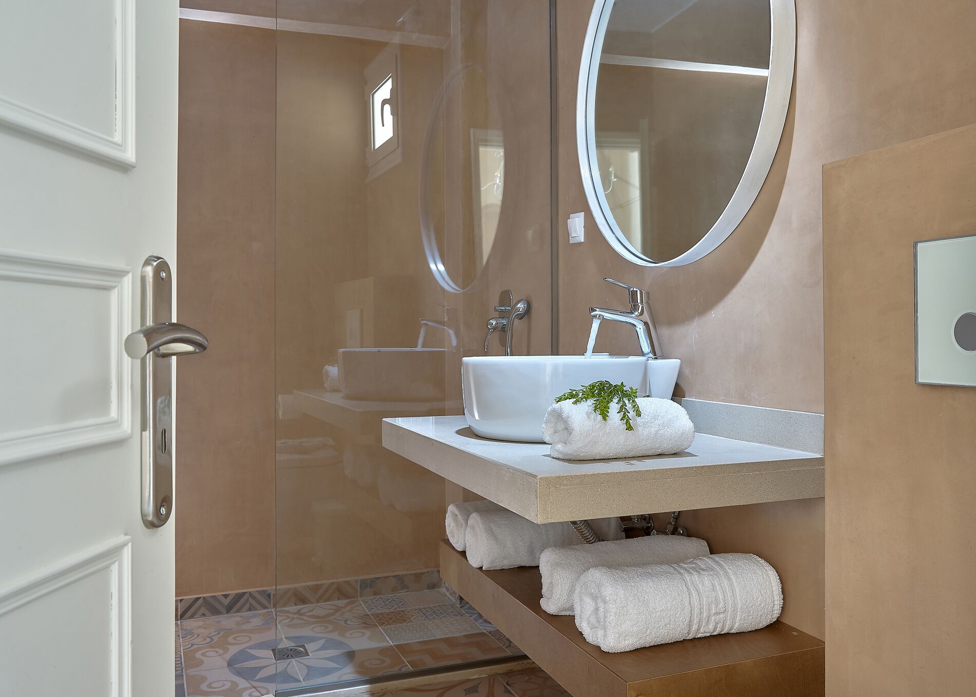 A modern bathroom with a glass shower door, a white sink, a mirror, and a towel rack with towels.