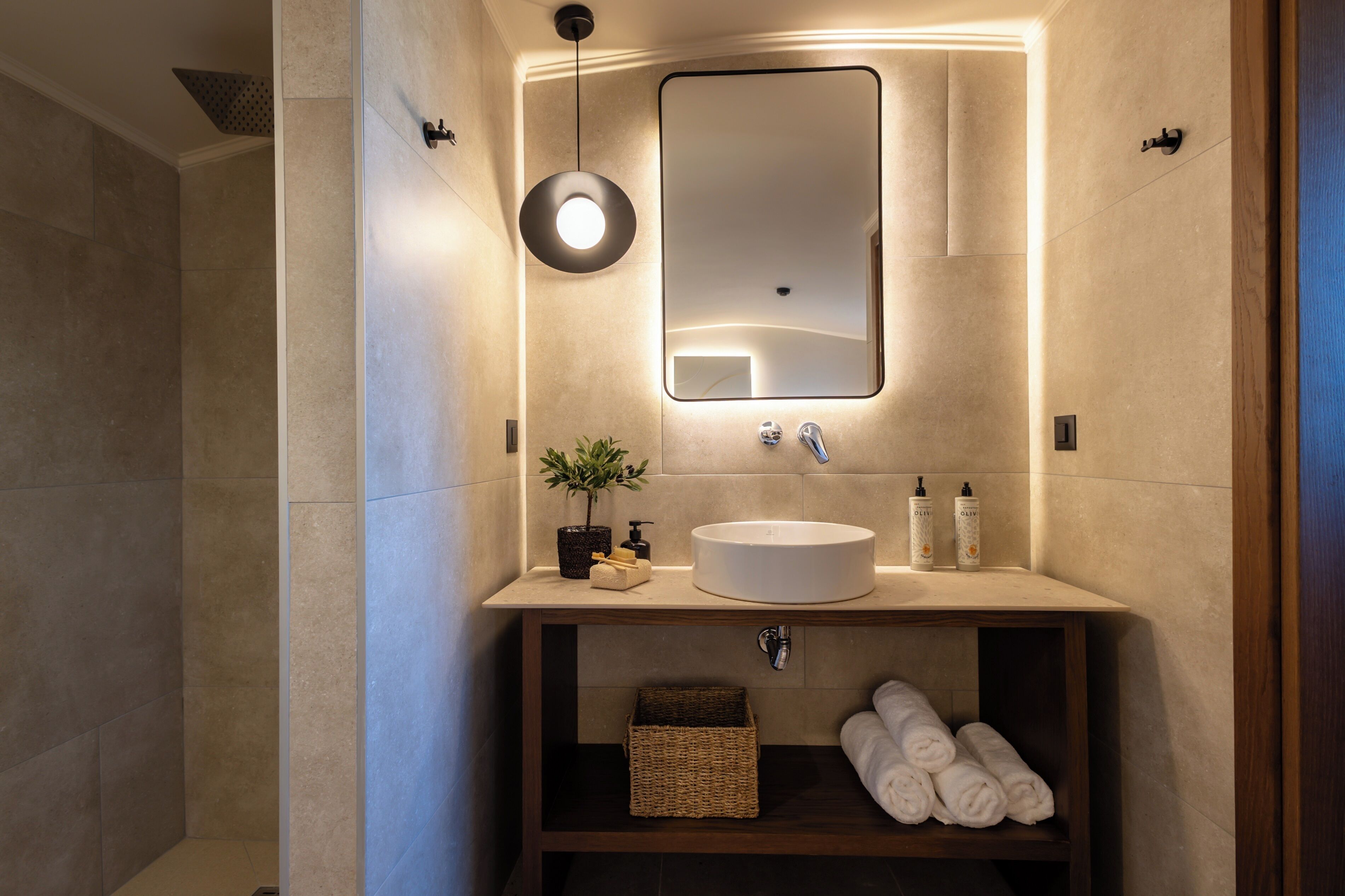 A modern bathroom with a large mirror, a round sink, and a shelf with towels and toiletries.