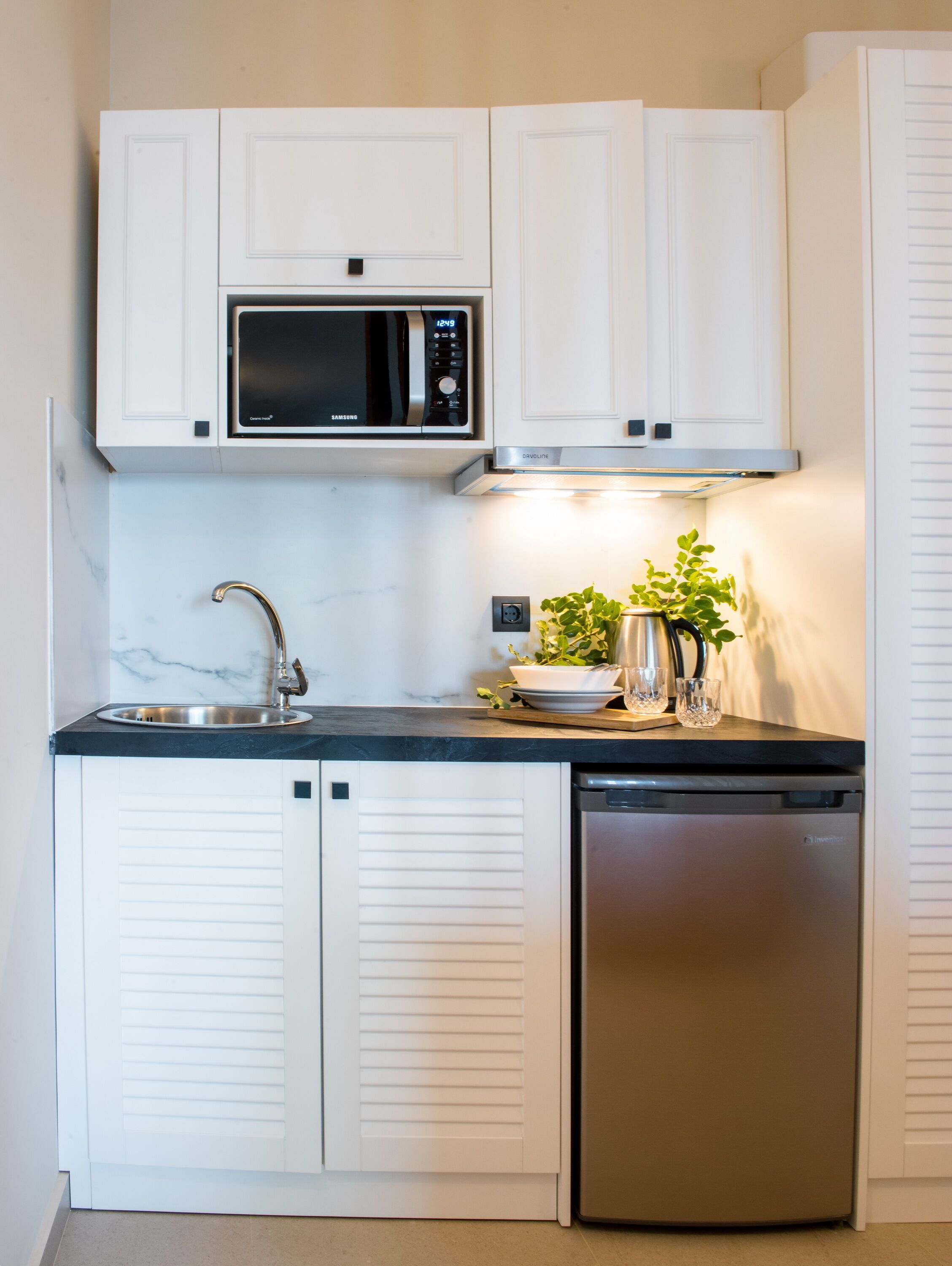 Una cocina compacta con armarios blancos, un lavamanos de acero inoxidable, un microondas y un lavavajillas.
