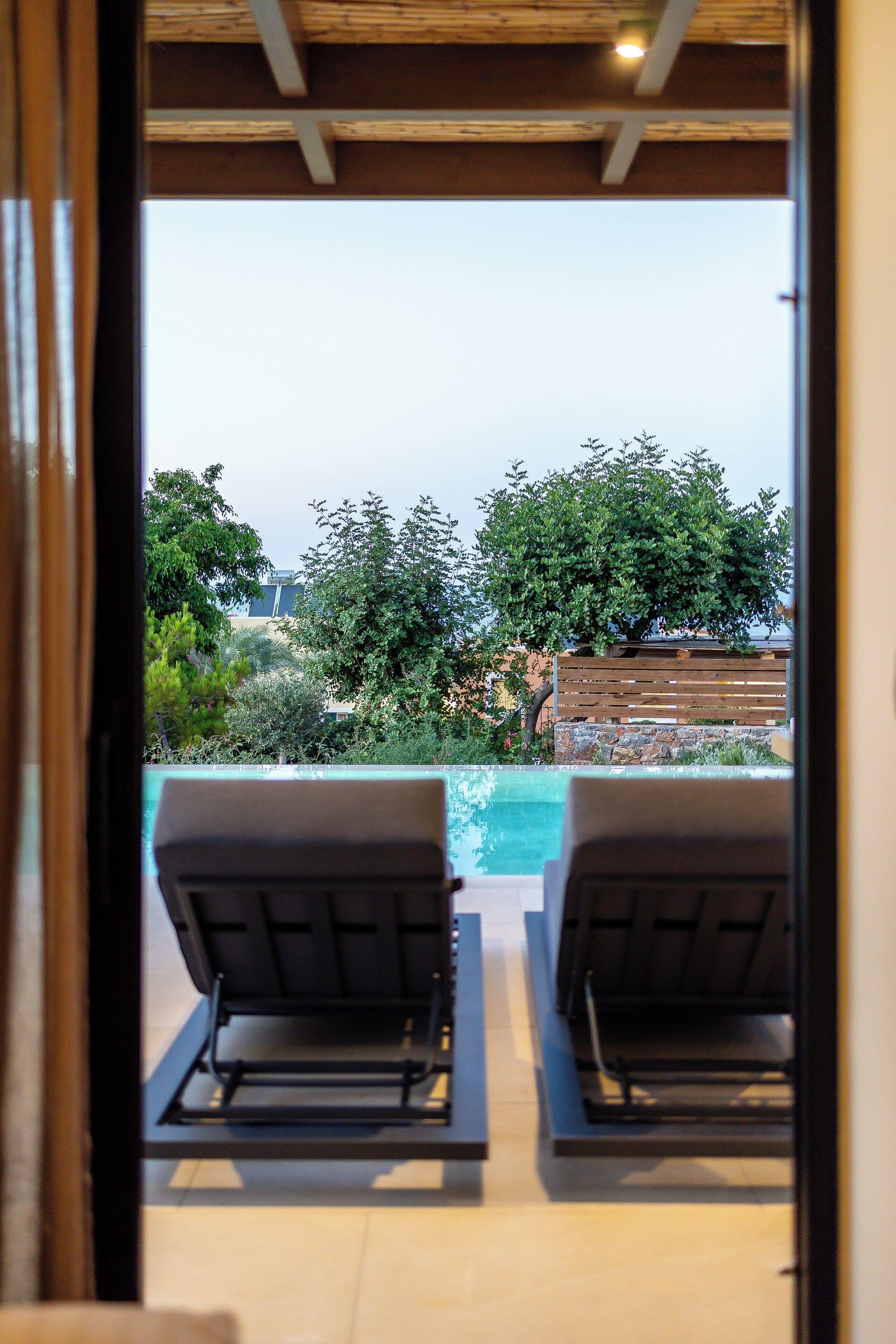 Vista desde un balcón con dos sillones de descanso mirando a una piscina, rodeado de follaje y un muro de piedra.
