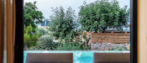 Vista desde un balcón con dos sillones de descanso mirando a una piscina, rodeado de follaje y un muro de piedra.