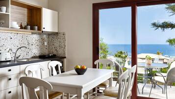 A modern kitchen with white cabinets, a speckled backsplash, and a dining area with a table and chairs. A bowl of fruit is on the table, and the room has a large sliding glass door leading to a patio with outdoor seating.