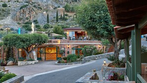 A rustic building with a stone facade, a covered outdoor seating area, and a view of a mountainous landscape. - Marni Village (Hersonissos)