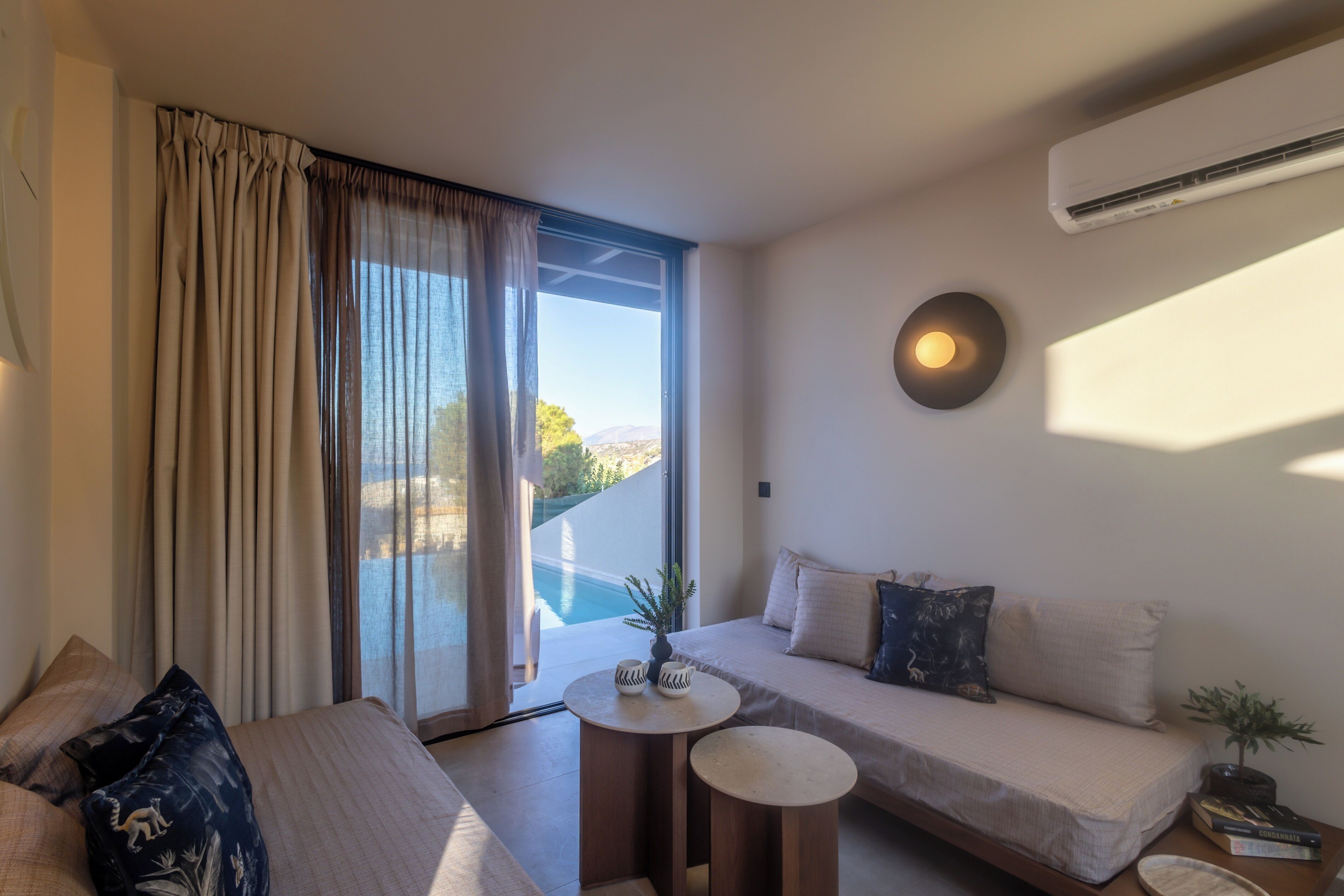 A modern hotel room with a large window, a sofa, a small round table, and a potted plant.