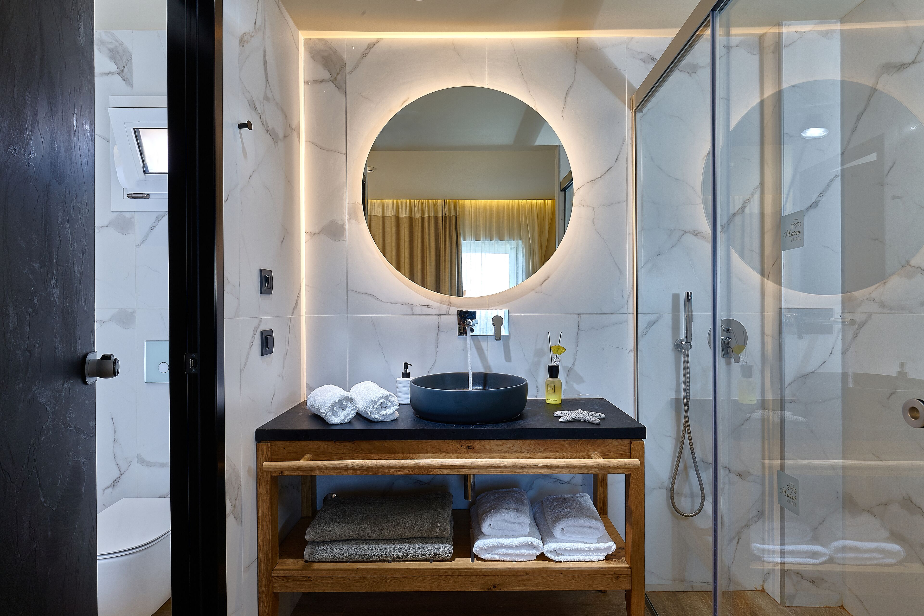 A modern bathroom with a round mirror, a black sink, and a glass-enclosed shower.