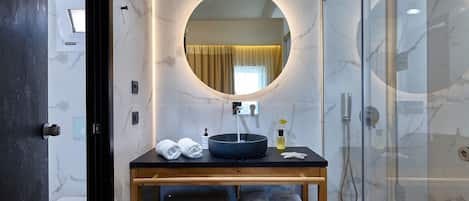 A modern bathroom with a round mirror, a black sink, and a glass-enclosed shower.