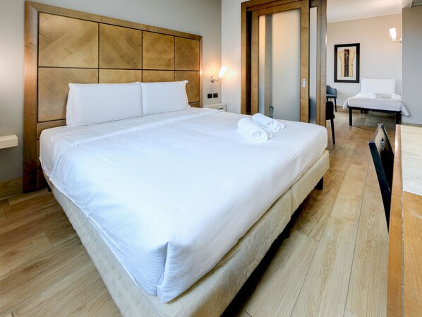 A neatly made bed with white linens and two rolled towels, a wooden headboard, and a wooden floor. - B&B Hotel Padova (Padova)