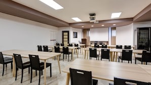 Kokoushuone, jossa on useita pöytiä ja tuoleja, projektorikangas ja esitysalue.