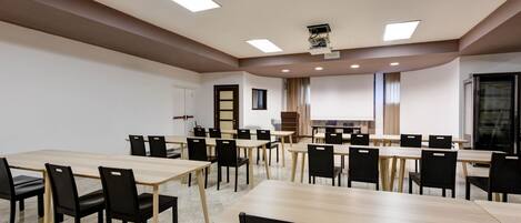 Un salón de conferencias con varias mesas y sillas, una pantalla de proyector y una zona para presentaciones.