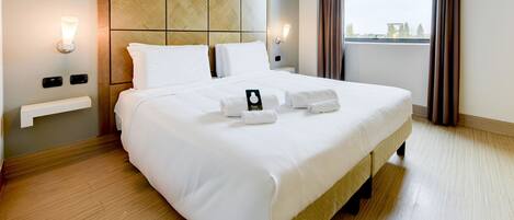 A neatly made bed with white linens, a wooden headboard, and a bedside table with a lamp.