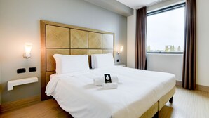 A neatly made bed with white linens, a wooden headboard, bedside lamps, and a view of the outdoors through a window with curtains. - B&B Hotel Padova (Padova)