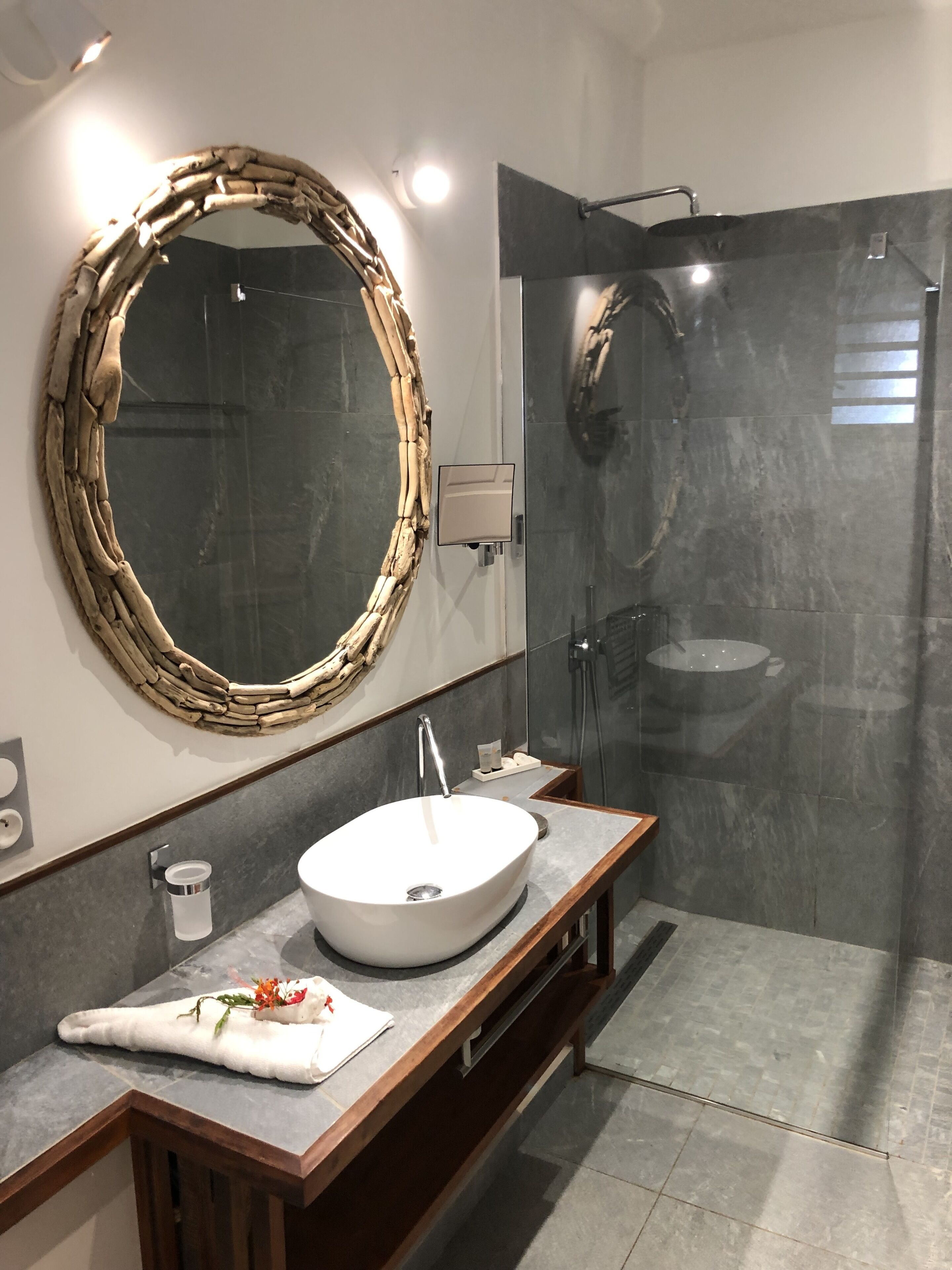 Une salle de bain moderne avec un miroir rond, un lavabo blanc et une douche à parois de verre.