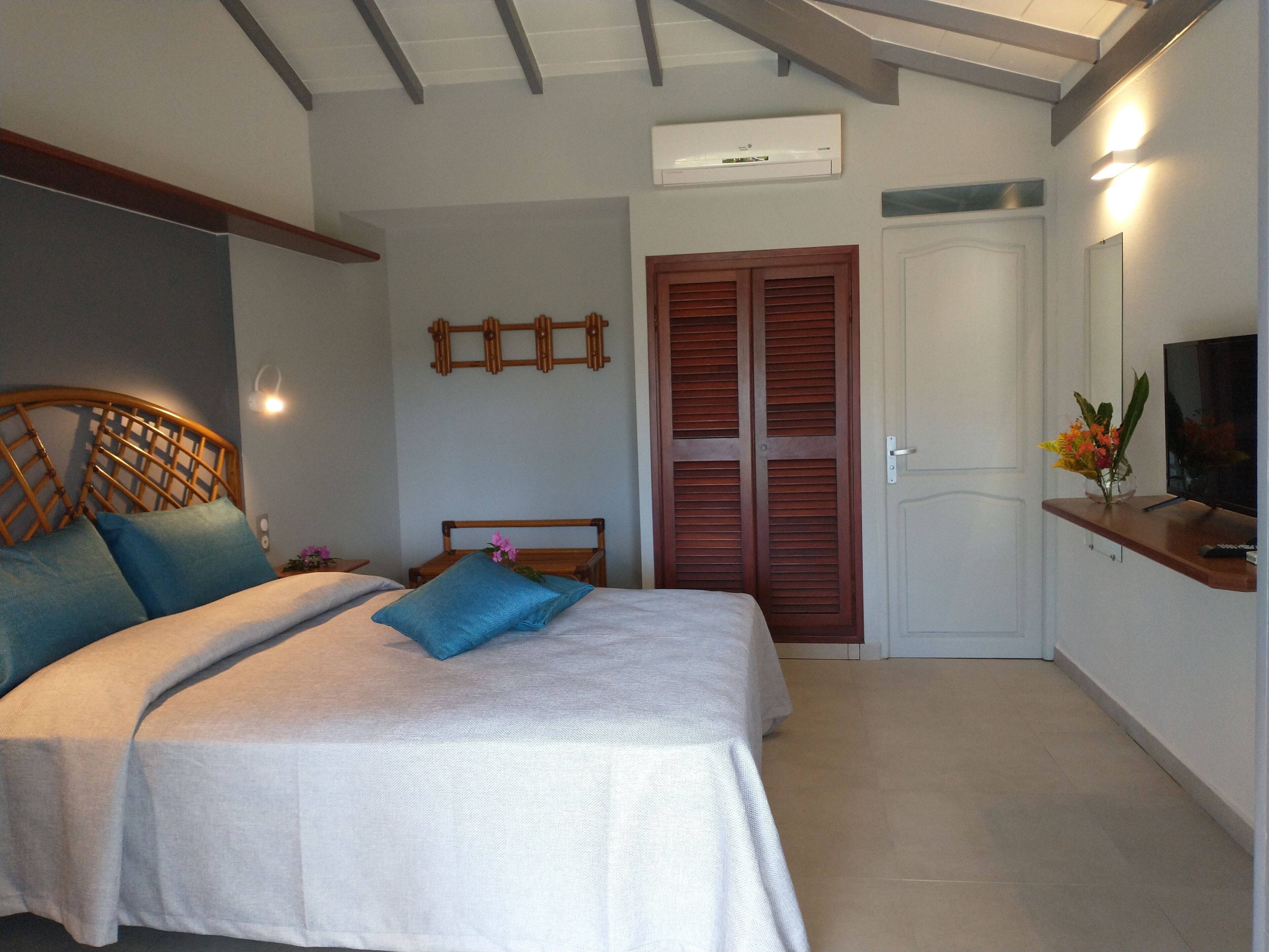 A bedroom with a bed, wooden headboard, a wall-mounted air conditioner, a TV on a shelf, and a door with a mirror.