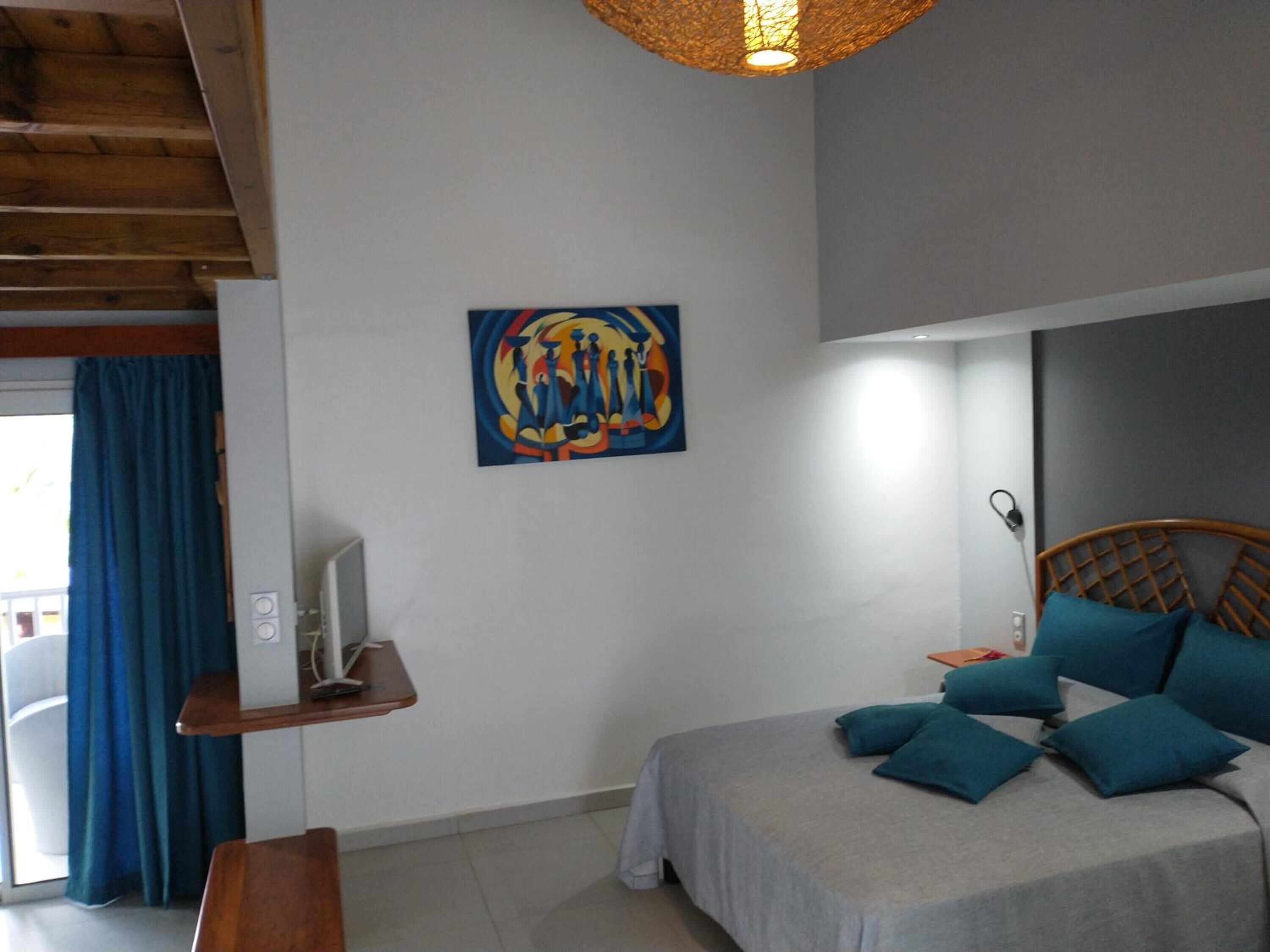 A bedroom with a bed, a desk, a chair, a television, and a painting on the wall.