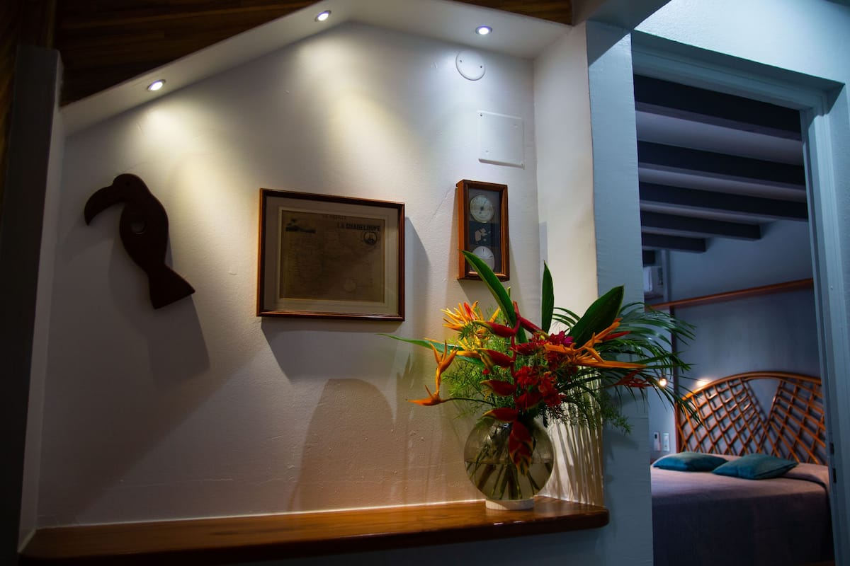 A room with a wooden headboard, a framed map on the wall, a clock, and a vase with flowers on a table.