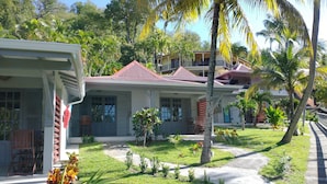 A two-story building with a red roof, surrounded by lush greenery and palm trees.