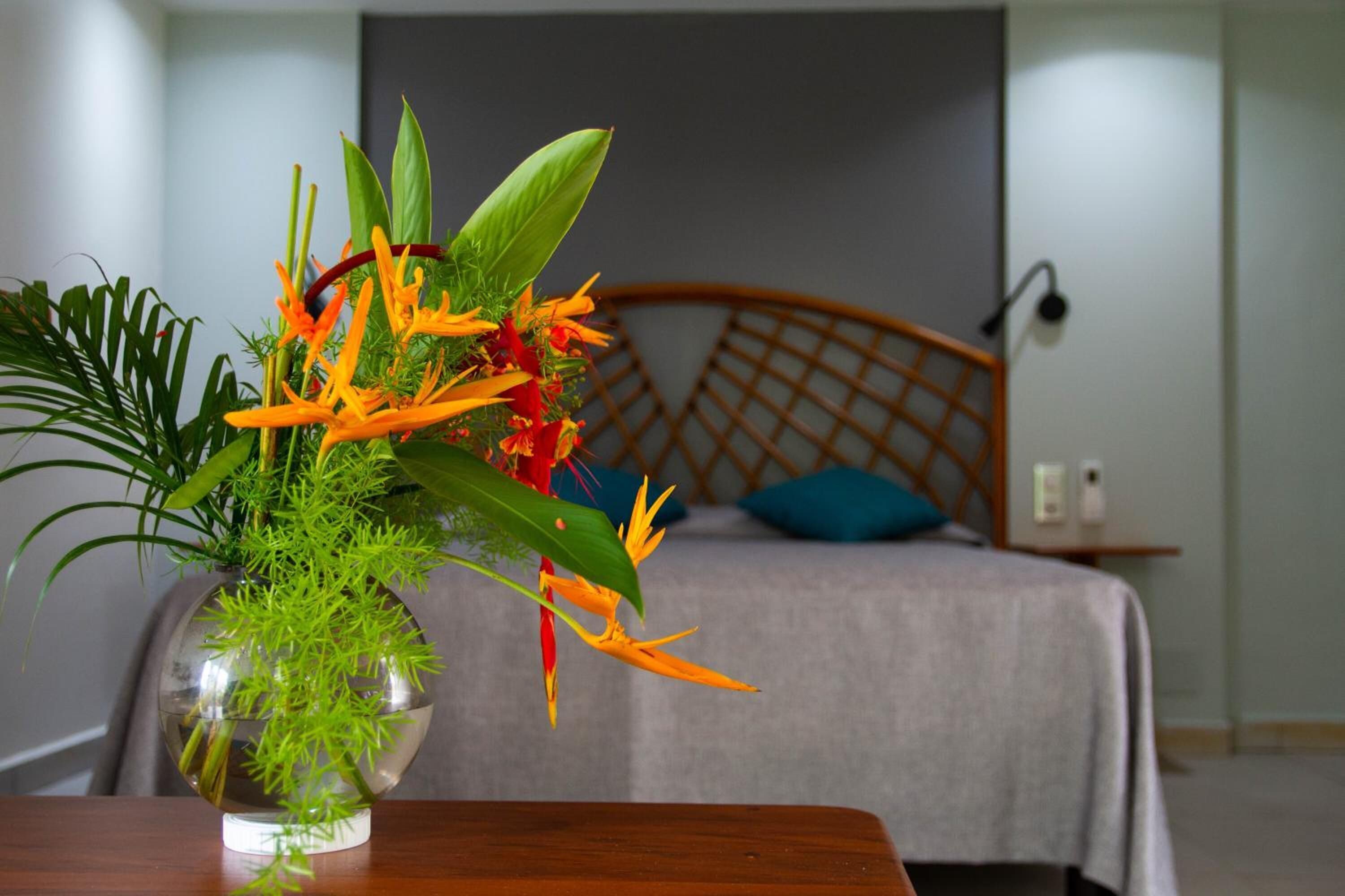 A bed with a wooden headboard, a bedside table, and a vase with a plant.