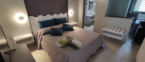 Une chambre à coucher moderne, avec un lit, des lampes de chevet et une salle de bain visible à travers une porte ouverte.