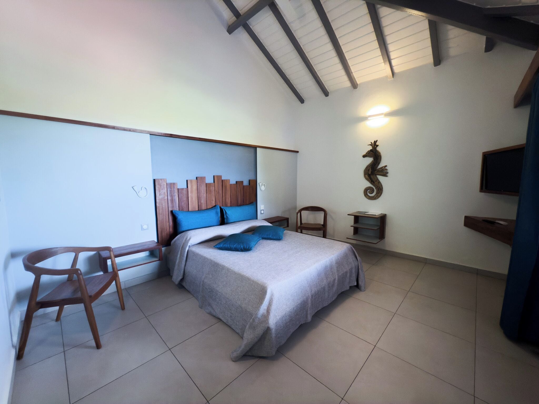 A bedroom with a bed, a chair, a desk, a wall-mounted shelf, and a decorative seahorse.