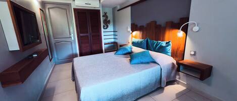 Un dormitorio con cama, mesitas de noche, televisor en la pared y una puerta.