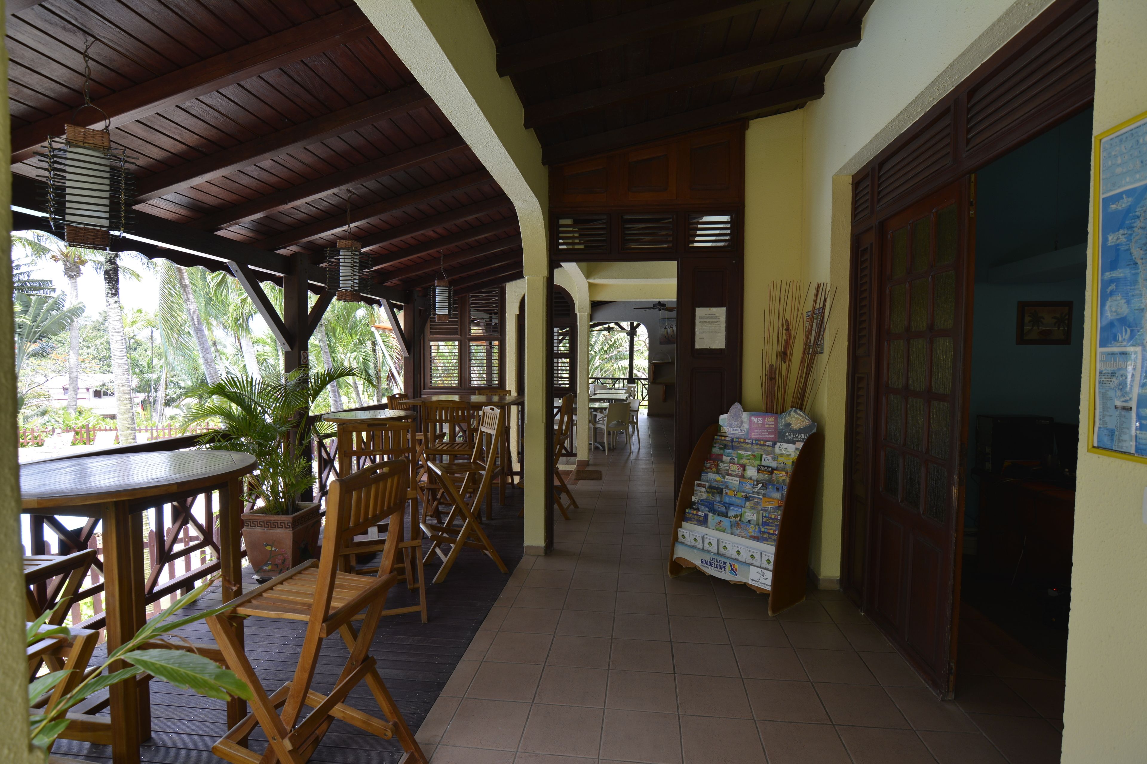 A covered outdoor seating area with wooden tables and chairs, a tiled floor, and a poster stand.